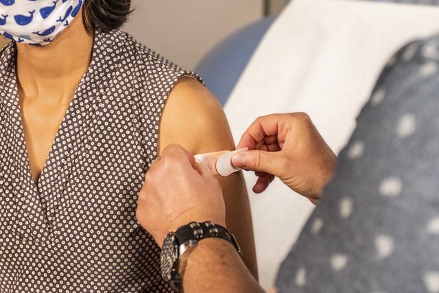 A person's hand putting a band-aid to a vaccinated woman's arm.