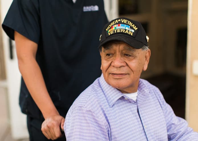 A caregiver assists an elderly veteran in a wheelchair.