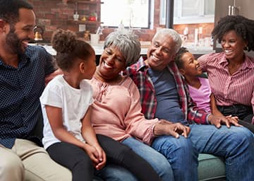 A family of parents and children sits on a couch and laughs with their grandparents.