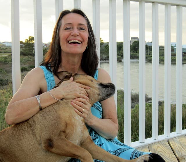 A laughing woman with a dog sits in front of a fence.