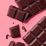 Pieces of milk chocolates on a pink surface.