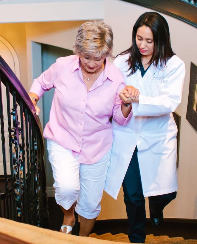 An Amada doctor assists an elderly woman as she moves up the stairs.