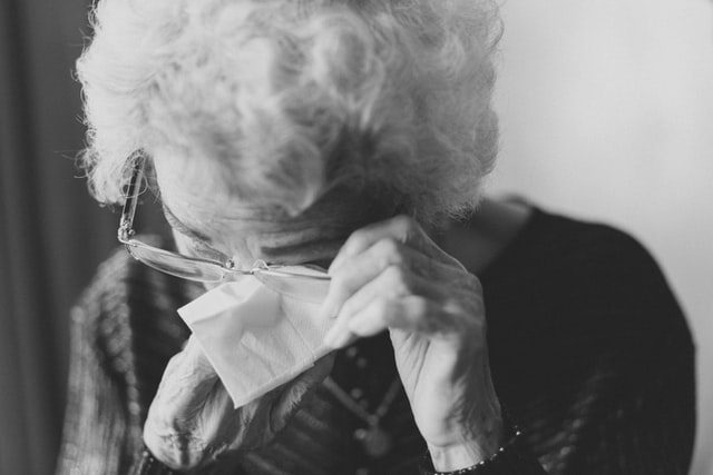 A close-up of an elderly woman wiping her tears with a napkin.