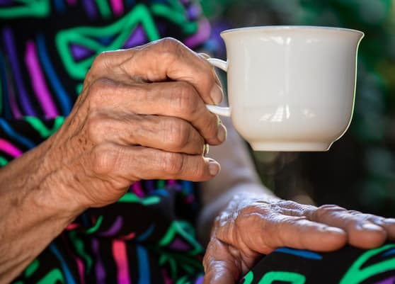An elderly woman's hand holding a teacup.