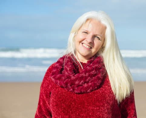 An elderly woman poses for the camera on the beach.