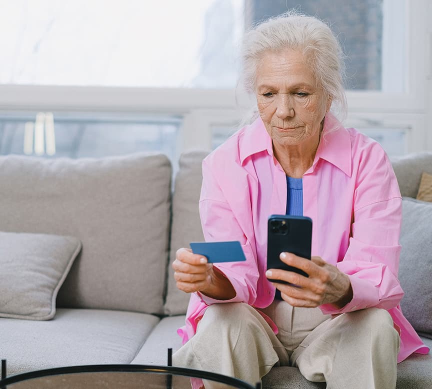 An elderly woman sitting on a couch holding her mobile and a calling card.