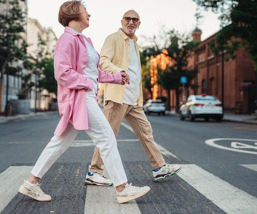 An elderly couple walks across the street holding hands.