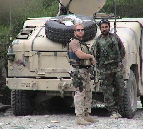 Two military personnel standing beside a military truck.