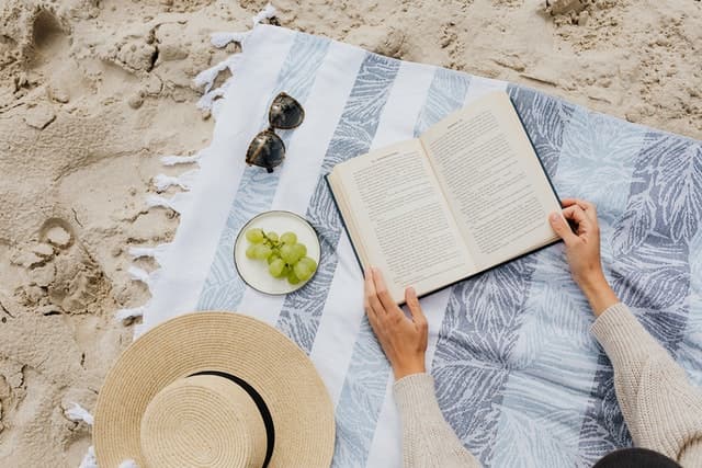 Reading a book by the beach on a beach mat.