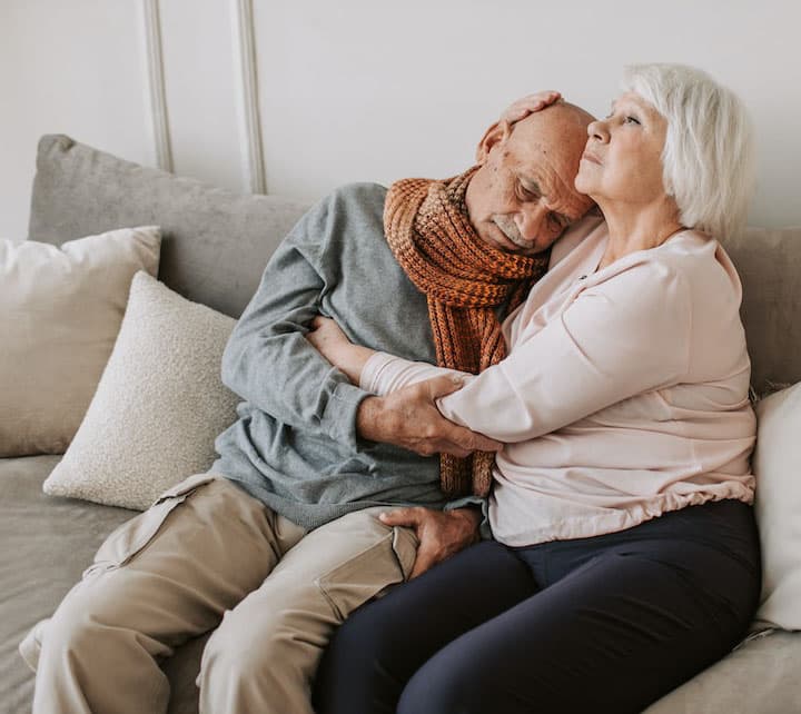 An elderly couple sitting on the couch embracing each other.